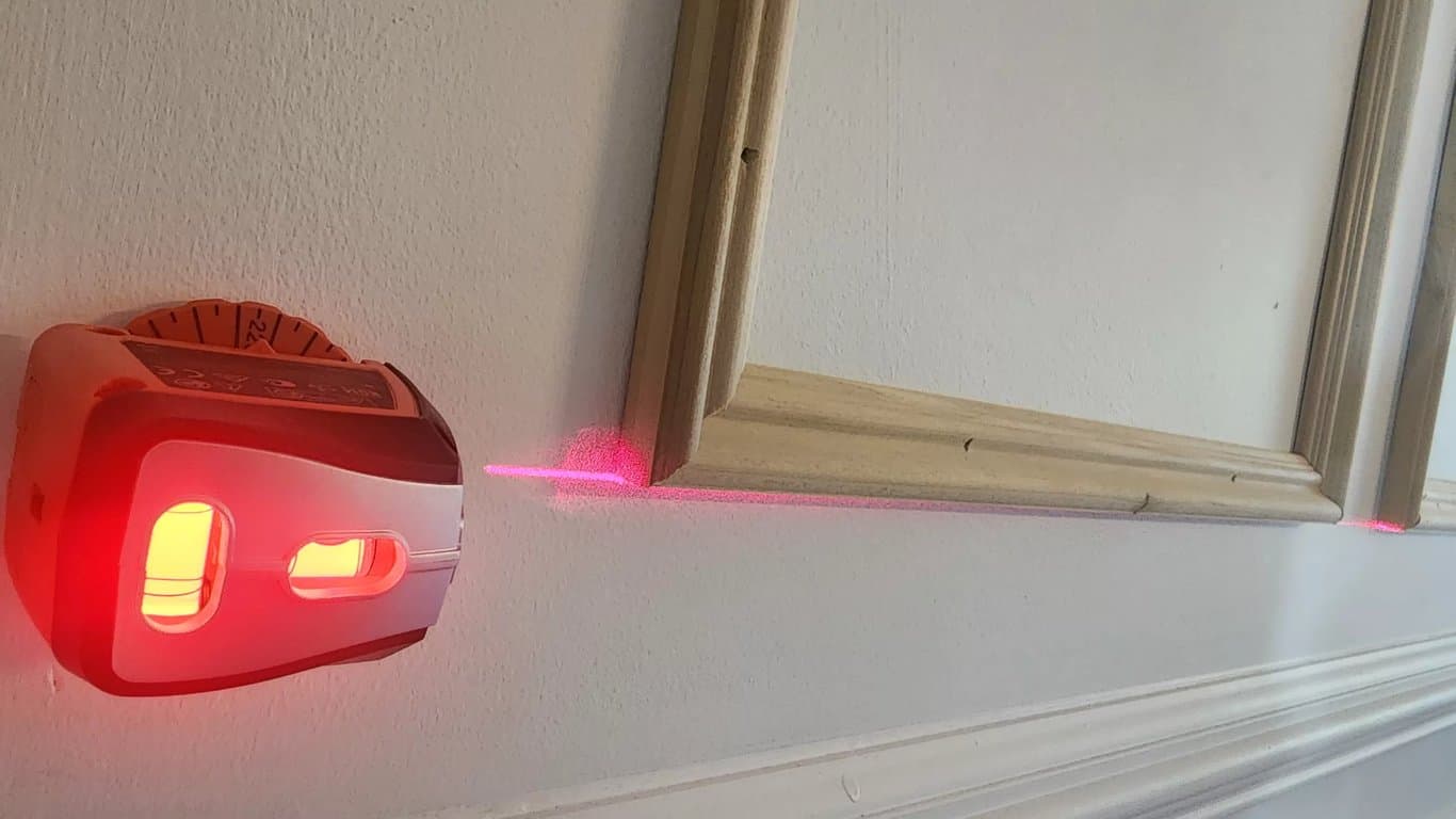 Laser level projecting a red guide line across unpainted picture-frame molding