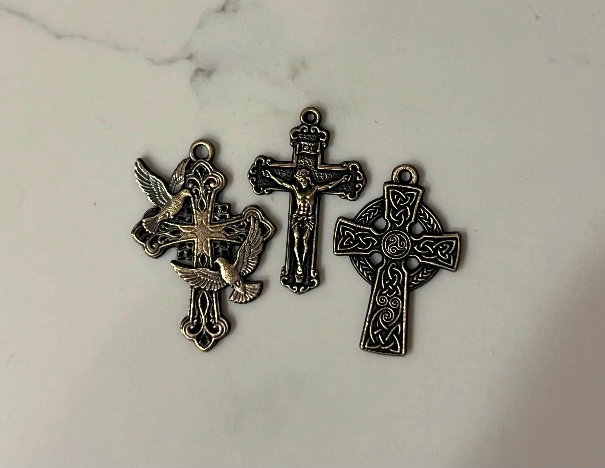 Three finished laser engraved cross pendants photographed together: a dove design, a crucifix, and a Celtic cross.